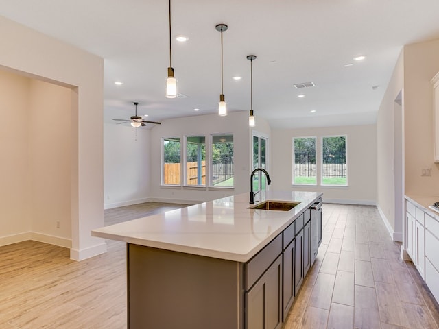 kitchen with light hardwood / wood-style flooring, sink, an island with sink, ceiling fan, and hanging light fixtures