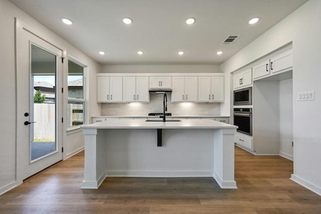 kitchen with white cabinetry, dark wood-type flooring, oven, and a kitchen island with sink