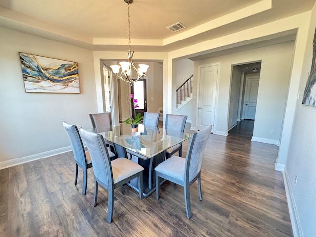 dining space featuring a chandelier, a tray ceiling, and dark wood-type flooring