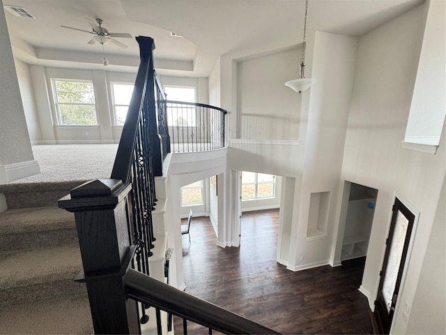 stairs with ceiling fan, a raised ceiling, wood-type flooring, and a towering ceiling