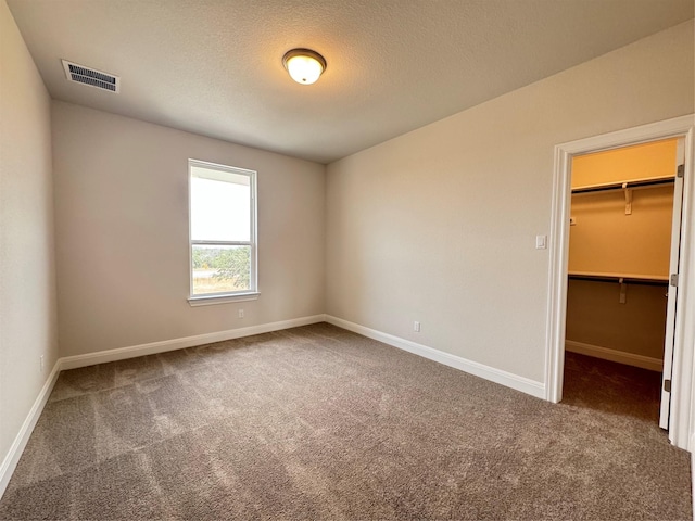 unfurnished bedroom with a walk in closet, a closet, dark carpet, and a textured ceiling