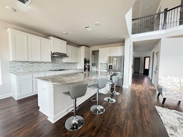 kitchen featuring stainless steel fridge with ice dispenser, an island with sink, black electric cooktop, decorative backsplash, and white cabinets