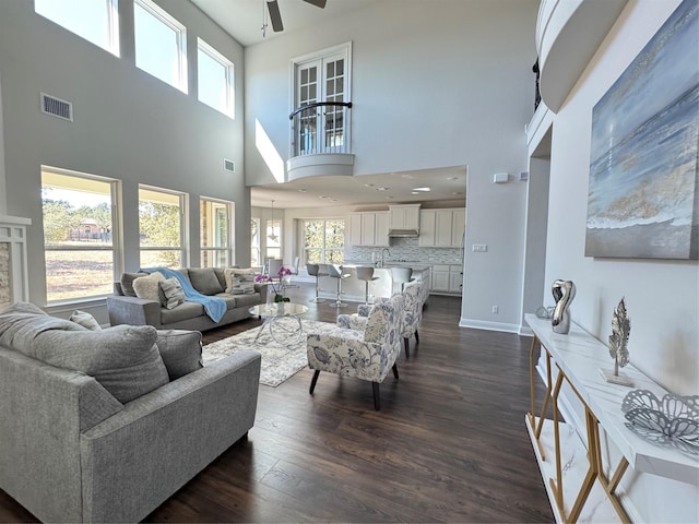 living room featuring ceiling fan, a towering ceiling, and dark wood-type flooring