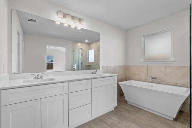 bathroom featuring plus walk in shower, vanity, and tile walls