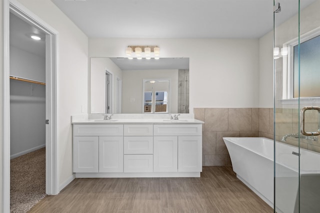 full bath with a walk in closet, double vanity, a stall shower, a sink, and a freestanding tub