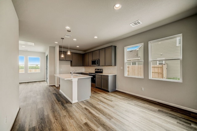 kitchen featuring decorative backsplash, a kitchen island with sink, decorative light fixtures, appliances with stainless steel finishes, and light hardwood / wood-style floors