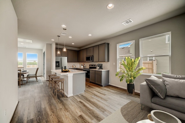 kitchen with a kitchen island, a breakfast bar area, decorative light fixtures, appliances with stainless steel finishes, and light hardwood / wood-style floors