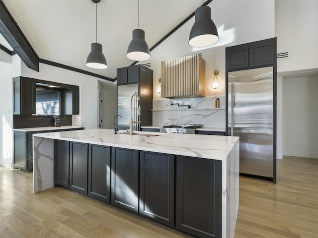 kitchen with a center island with sink, built in refrigerator, pendant lighting, and light hardwood / wood-style floors