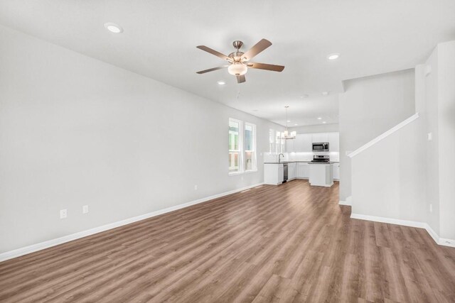 unfurnished living room featuring sink, ceiling fan with notable chandelier, and light wood-type flooring