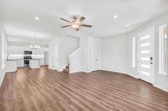 unfurnished living room featuring sink, ceiling fan with notable chandelier, and light hardwood / wood-style floors