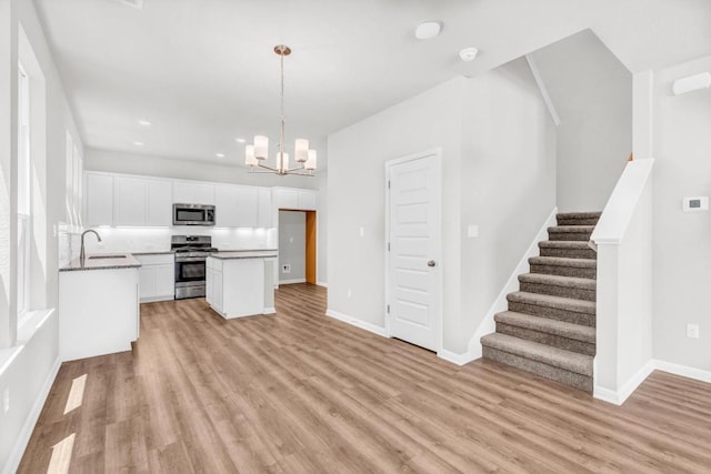 kitchen with sink, white cabinetry, hanging light fixtures, stainless steel appliances, and light wood-type flooring