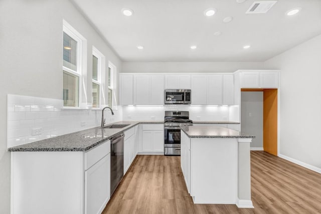 kitchen with sink, appliances with stainless steel finishes, white cabinets, a kitchen island, and dark stone counters