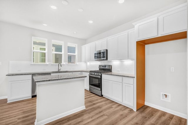 kitchen featuring white cabinetry, stainless steel appliances, a center island, and light stone counters