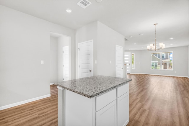 kitchen featuring pendant lighting, white cabinets, an inviting chandelier, light stone countertops, and light hardwood / wood-style flooring