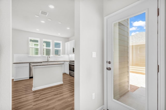 kitchen featuring sink, stainless steel range with gas cooktop, white cabinetry, and light hardwood / wood-style flooring