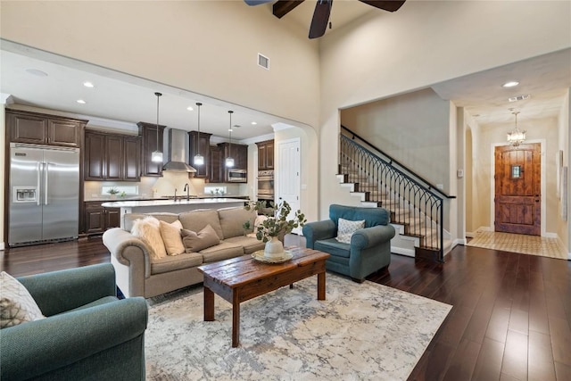 living room with ceiling fan with notable chandelier, a high ceiling, dark hardwood / wood-style flooring, and sink