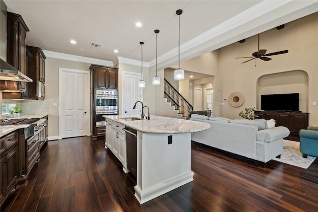 kitchen with ceiling fan, hanging light fixtures, backsplash, a kitchen island with sink, and appliances with stainless steel finishes