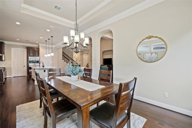 dining room featuring a tray ceiling, crown molding, dark wood-type flooring, and a notable chandelier