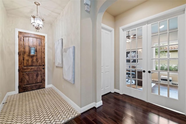 foyer entrance with dark wood-style flooring, a chandelier, baseboards, arched walkways, and french doors