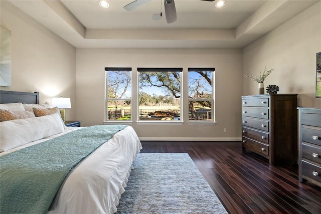 bedroom with ceiling fan, dark hardwood / wood-style floors, and a tray ceiling