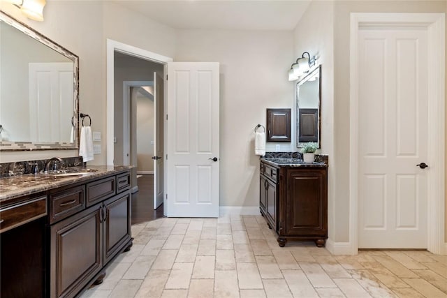 full bath featuring baseboards, two vanities, and a sink