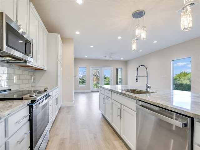 kitchen with stainless steel appliances, light stone countertops, light hardwood / wood-style flooring, white cabinets, and backsplash