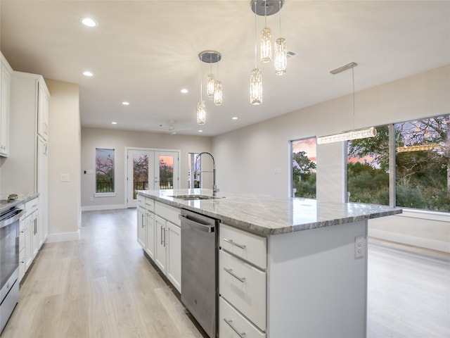 kitchen with white cabinetry, light wood-type flooring, a kitchen island with sink, light stone countertops, and hanging light fixtures