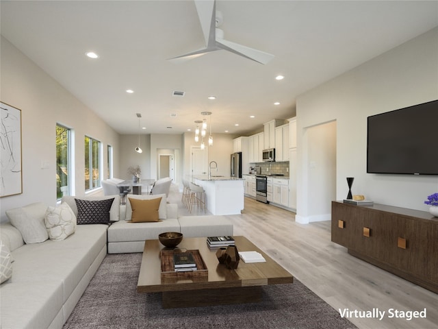 living room featuring ceiling fan, light hardwood / wood-style flooring, and sink