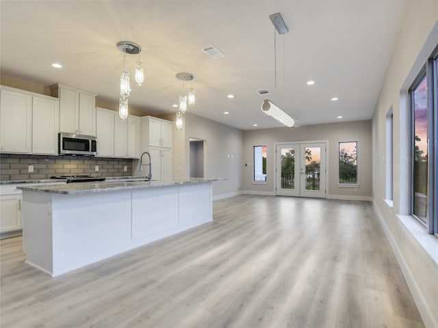 kitchen with pendant lighting, light stone countertops, light hardwood / wood-style flooring, and white cabinetry