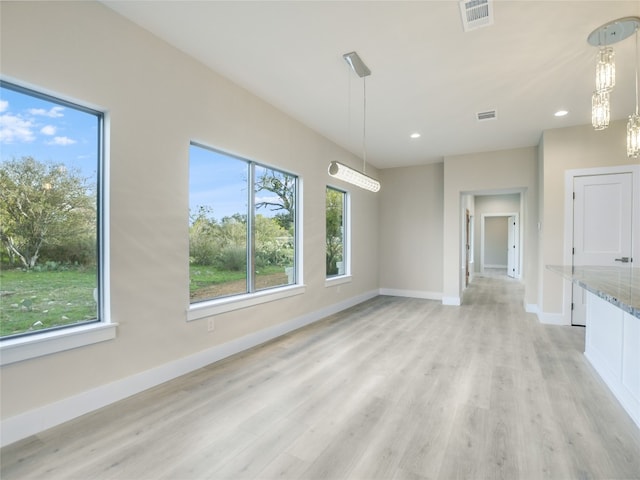 unfurnished living room with an inviting chandelier, a wealth of natural light, and light hardwood / wood-style floors