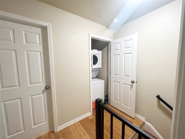 corridor with stacked washer and clothes dryer and light hardwood / wood-style floors