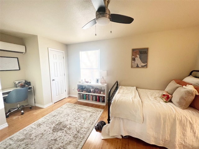 bedroom featuring ceiling fan, a wall mounted AC, and light hardwood / wood-style floors