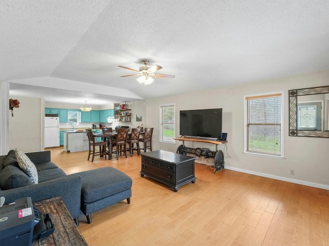 living room with ceiling fan, sink, vaulted ceiling, a textured ceiling, and light wood-type flooring