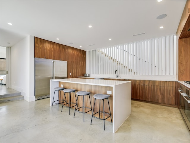 kitchen featuring a kitchen island, a kitchen bar, gas cooktop, high end refrigerator, and sink