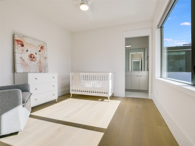 unfurnished bedroom featuring a nursery area, ceiling fan, radiator, and light wood-type flooring