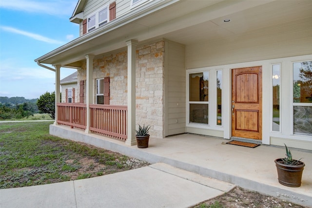 view of exterior entry with a lawn and a porch