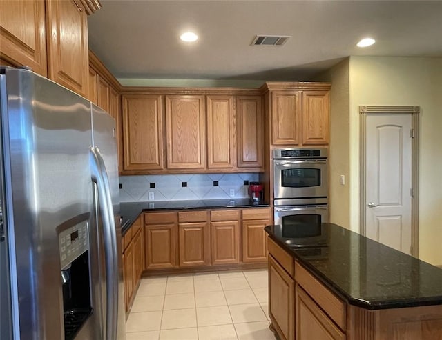 kitchen with light tile patterned flooring, stainless steel appliances, dark stone counters, and tasteful backsplash