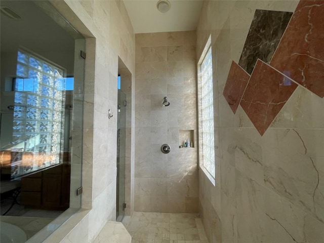 bathroom featuring a tile shower, a wealth of natural light, and tile walls