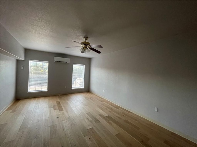 spare room featuring a textured ceiling, light hardwood / wood-style floors, an AC wall unit, and ceiling fan