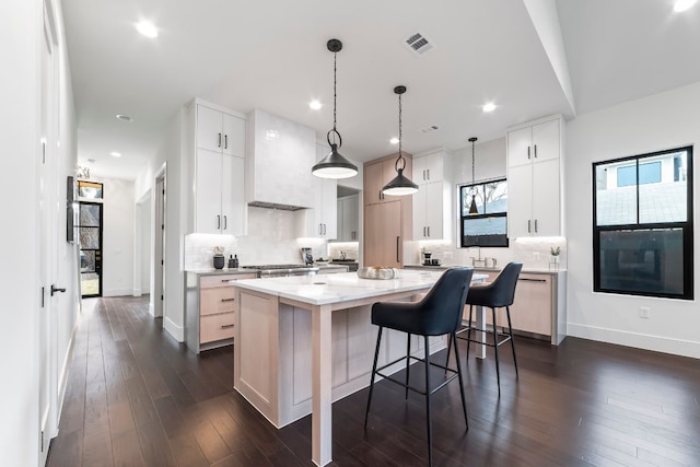 kitchen featuring hanging light fixtures, dark hardwood / wood-style floors, custom range hood, a kitchen island, and white cabinetry