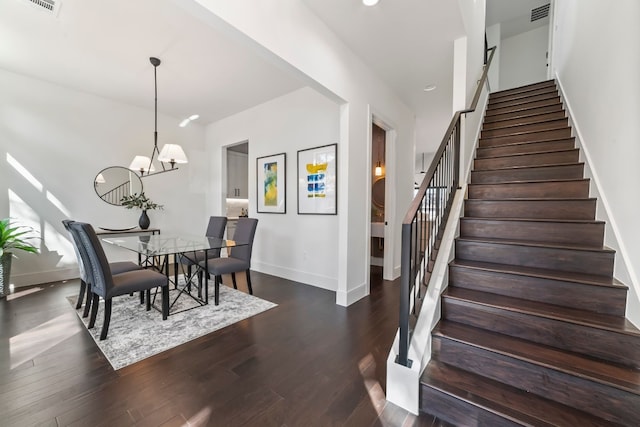 stairs with hardwood / wood-style floors and an inviting chandelier