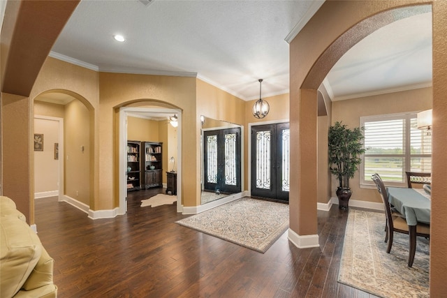 foyer entrance featuring french doors, a chandelier, crown molding, and dark wood-type flooring