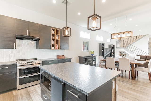 kitchen with pendant lighting, stainless steel appliances, a kitchen island, tasteful backsplash, and light wood-type flooring