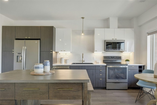 kitchen with backsplash, hanging light fixtures, white cabinets, sink, and appliances with stainless steel finishes