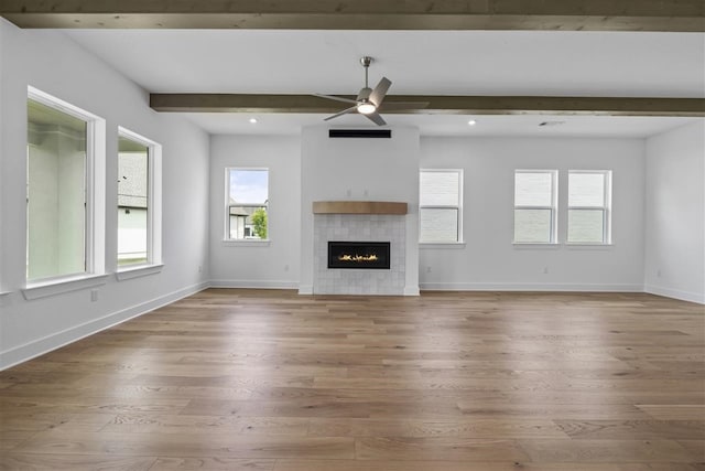 unfurnished living room with ceiling fan, hardwood / wood-style flooring, a tiled fireplace, and beamed ceiling