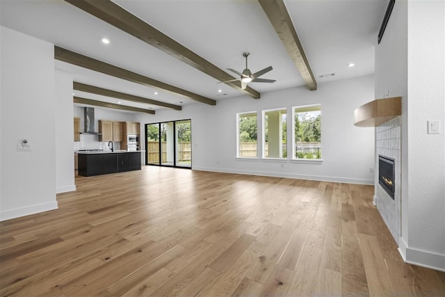 unfurnished living room featuring beamed ceiling, ceiling fan, light hardwood / wood-style floors, and a fireplace