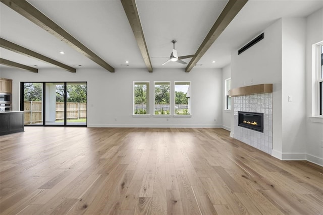 unfurnished living room with light hardwood / wood-style floors, ceiling fan, a healthy amount of sunlight, and beam ceiling