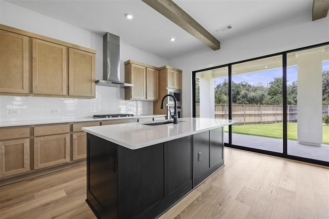 kitchen featuring sink, tasteful backsplash, beam ceiling, an island with sink, and wall chimney range hood