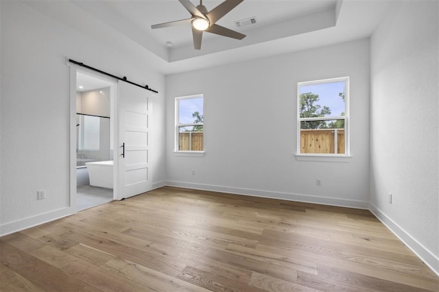 unfurnished bedroom featuring ensuite bathroom, light hardwood / wood-style floors, a barn door, and ceiling fan