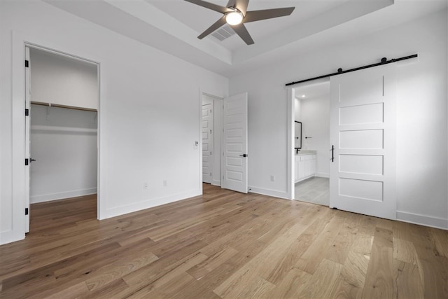 unfurnished bedroom with ensuite bath, ceiling fan, a spacious closet, a barn door, and light wood-type flooring